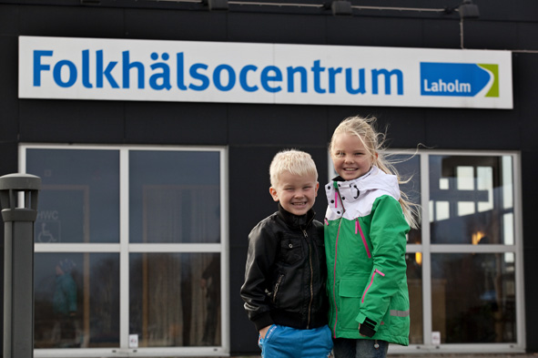 Två barn en kille och en tjej framför Folkhälsocentrums logotyp Fotograf Christel Lind